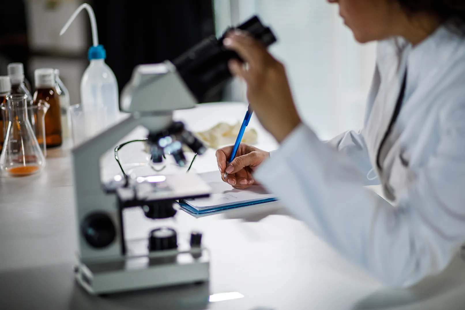 Female scientist writing notes on a clipboard after analyzing samples under a microscope 