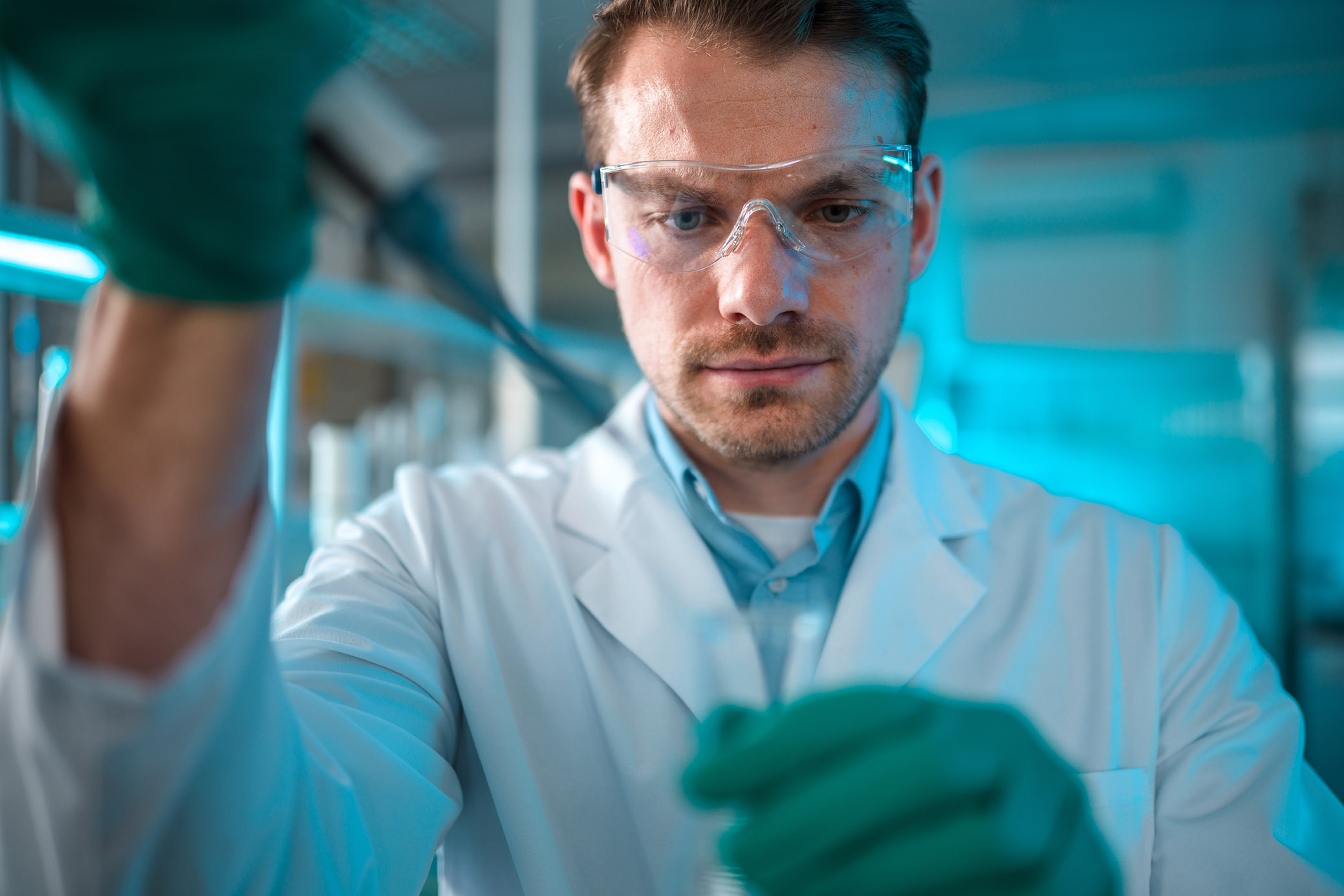 Male lab employee wearing protective gloves, glasses and a lab coat