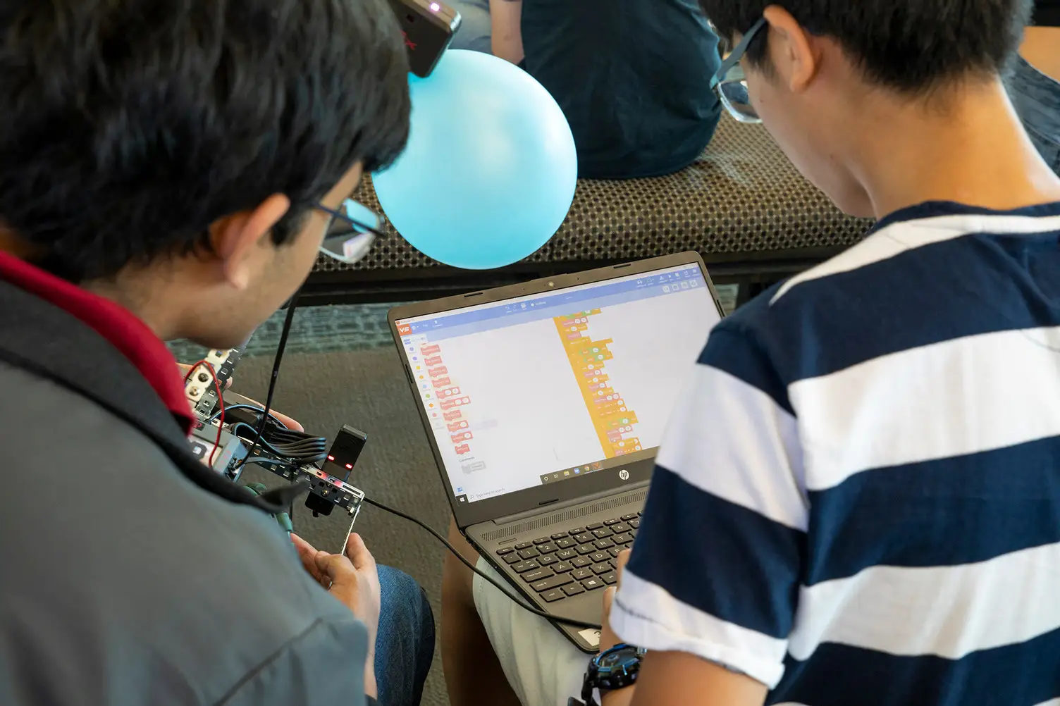 Two male students code on a laptop computer