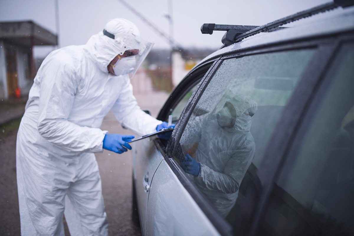 A medical professional wearing personal protective equipment talks to a person in a car