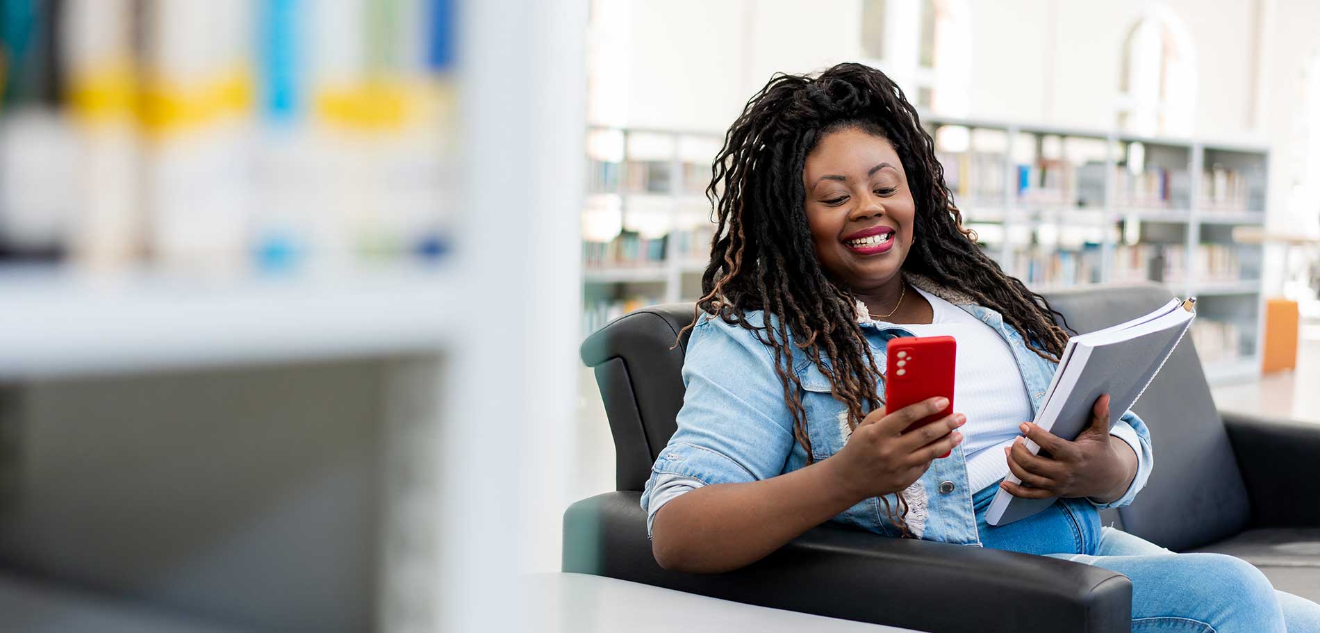image of a woman sitting in a chair looking at her phone with an expression of delight on her face